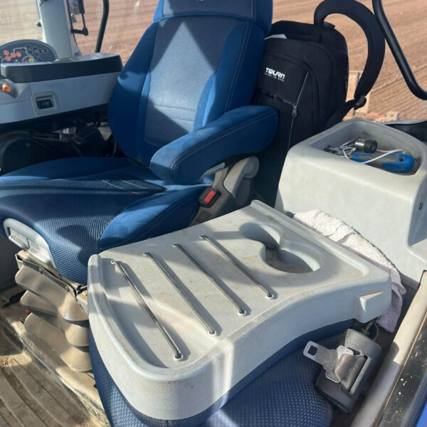 Blue tractor cabin seat with a black TOUR backpack resting beside it; field visible through the window in the background.