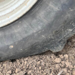 Close-up of a dirty black tire next to a white, rusted wheel rim on rocky, dirt ground.