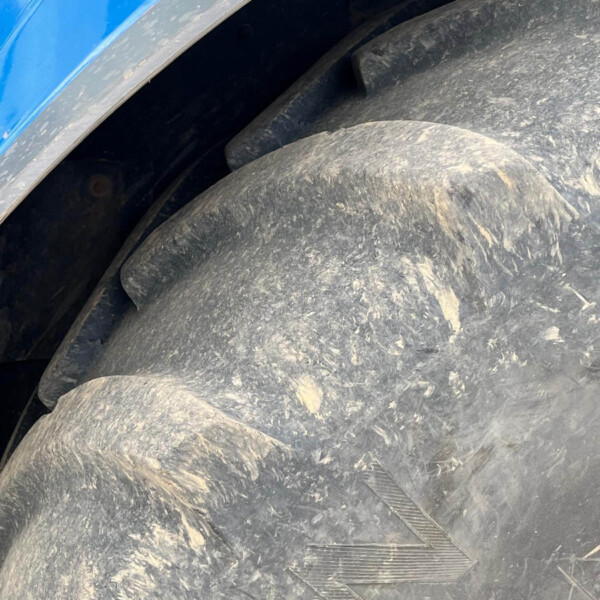 Close-up of a muddy tire with deep tread and a blue vehicle body visible in the corner.