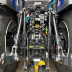 Close-up of the control panel and hydraulic levers inside a combine harvester, with colored knobs and cables between large tires."ss"