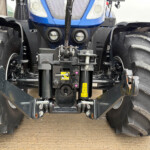 Close-up of a New Holland tractor front hitch with hydraulic linkage and dual large tread tires on either side.
