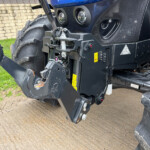 Close-up of a heavy-duty tractor front hitch and hydraulic linkage with warning labels and metal components
