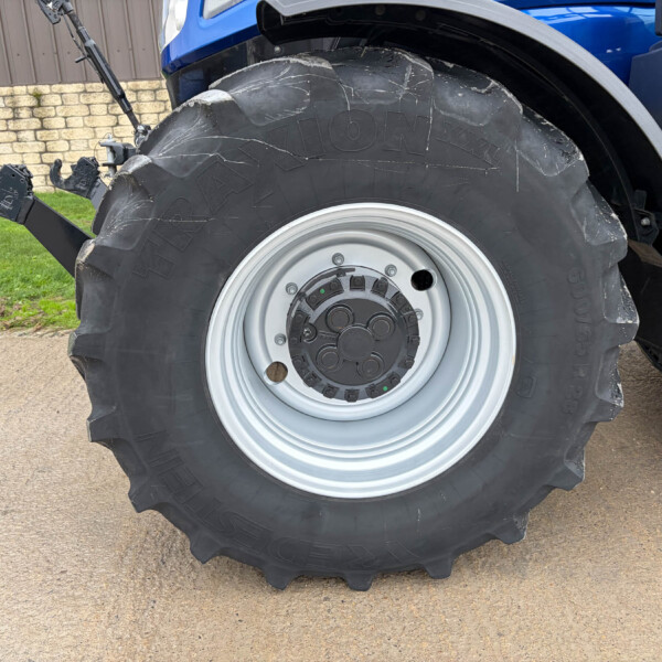 Close-up of a tractor rear tire and wheel with hitch, outdoor setting against a brick wall and grass in the background.
