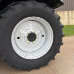 Close-up of a large tractor tire with a white rim, dirt on the treads, on a paved surface with a fence in the background.