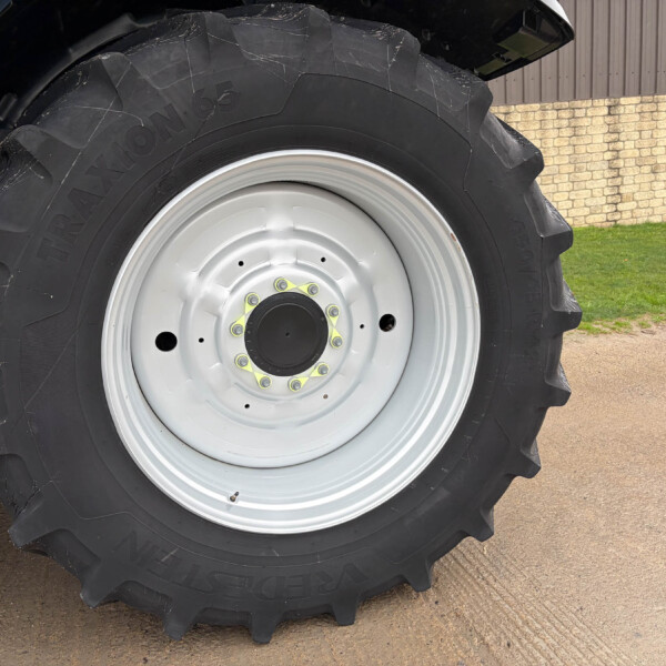 Close-up of a large tractor tire with a white rim, dirt on the treads, on a paved surface with a fence in the background.