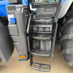 Close-up of a large truck cab entry: black metal steps, muddy tires, and the blue truck body beside the door area.