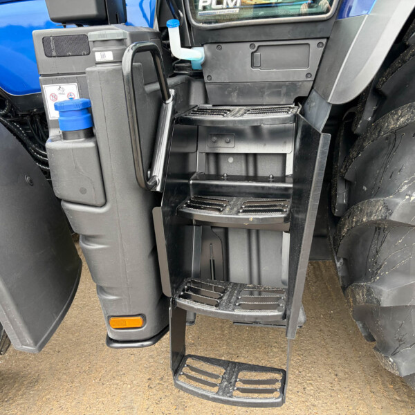 Close-up of a large truck cab entry: black metal steps, muddy tires, and the blue truck body beside the door area.