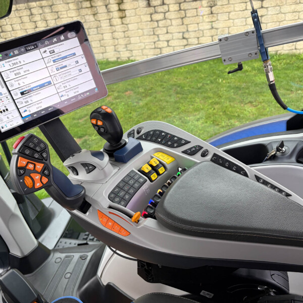 Cab interior of a tractor with a mounted tablet displaying engine data and controls, plus joystick and dashboard buttons.