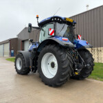 Blue tractor with large front tire and cab parked outside a brown industrial building, daytime. (informative)