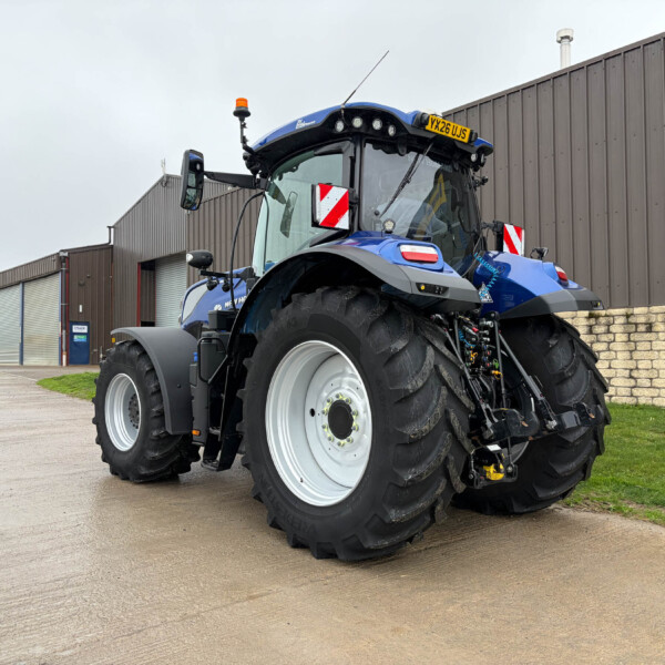 Blue tractor with large front tire and cab parked outside a brown industrial building, daytime. (informative)