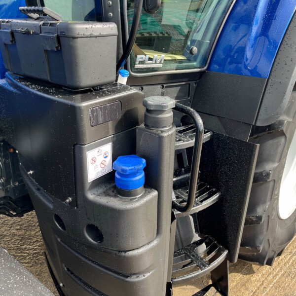 Front-left view of a blue New Holland tractor showing a black hydraulic unit, blue reservoir caps, and the PLM badge on the windshield.