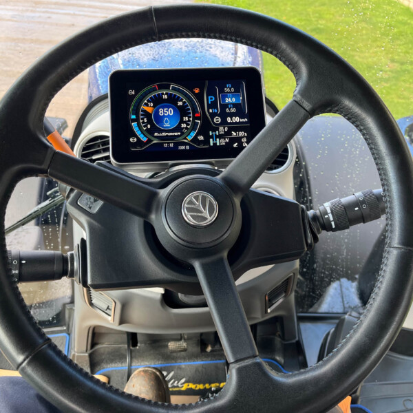 Interior view of a tractor cab with a circular digital gauge reading 850 and the steering wheel in front.