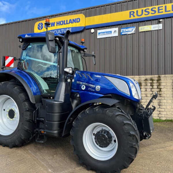Blue New Holland agricultural tractor parked outside a dealership with yellow building signs in the background
