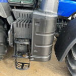 Close-up of black plastic steps and surrounding cab area of a blue truck, wet with raindrops and mud on the tires nearby.