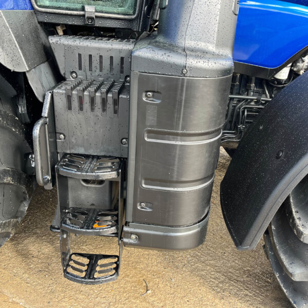 Close-up of black plastic steps and surrounding cab area of a blue truck, wet with raindrops and mud on the tires nearby.