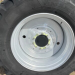Close-up of a large tractor tire mounted on a gray wheel with yellow bolts and deep treads visible.