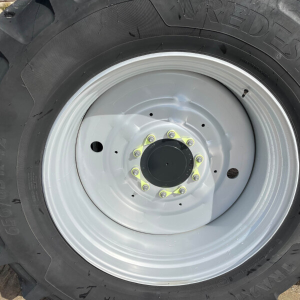Close-up of a large tractor tire mounted on a gray wheel with yellow bolts and deep treads visible.