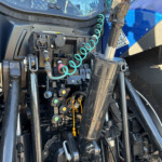 Close-up of a blue tractor’s hydraulic control module with levers, hoses, and a coiled green hose visible in the cab area