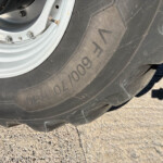 Close-up of a vehicle tire and silver wheel rim with a valve stem, resting on a rough concrete surface.