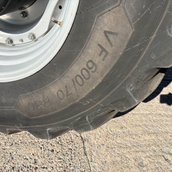 Close-up of a vehicle tire and silver wheel rim with a valve stem, resting on a rough concrete surface.