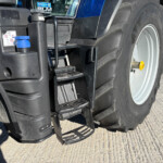 Close-up of a blue tractor showing its entry steps, hydraulic components, and a large rear tire.