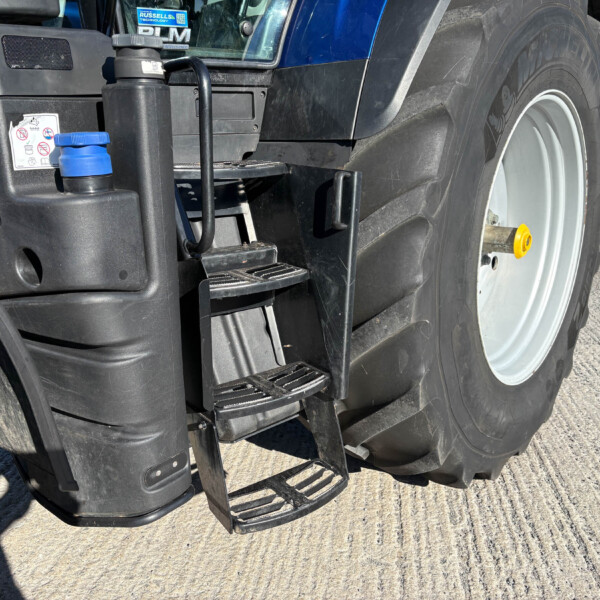 Close-up of a blue tractor showing its entry steps, hydraulic components, and a large rear tire.