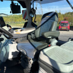 Inside a modern truck cab with a blue-trimmed driver’s seat, a tablet mounted on the left, and a parking lot visible through the windshield.