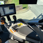 Inside a tractor cab with a mounted tablet showing control settings and gauges on a screen.
