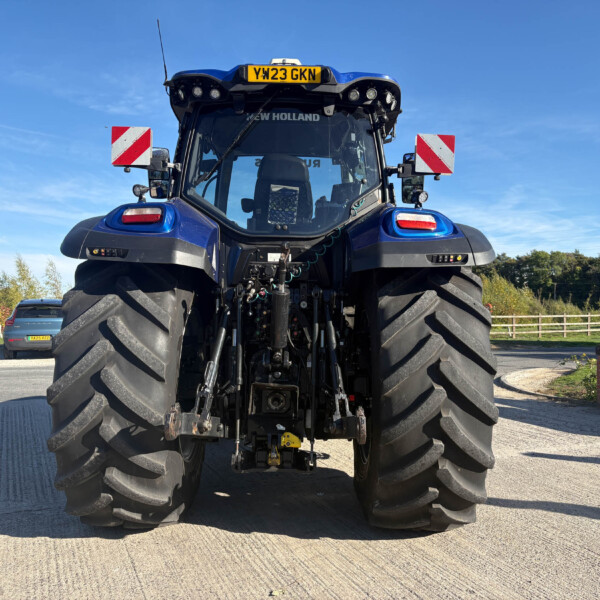Front view of a blue New Holland tractor with large rear tires and a yellow license plate reading YW23 GKN, in an outdoor lot.