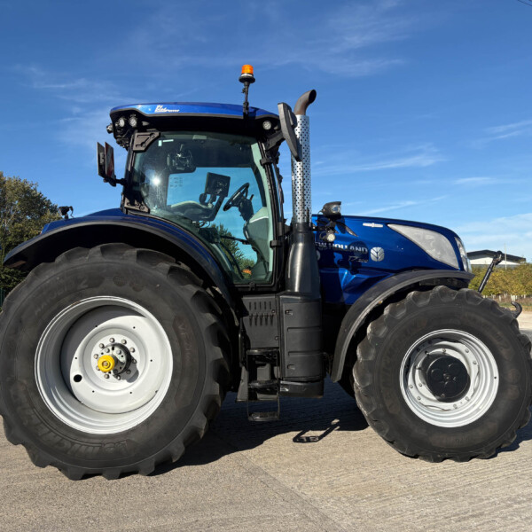 Blue New Holland tractor from a low front-left angle with oversized tires and an orange beacon on top.