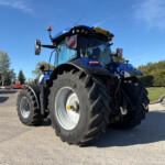 Close-up view of a blue tractor from the front-left, with large tires and a clear blue sky above.