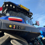 Close-up view of a blue truck cabin with a control panel showing various buttons and a yellow emergency stop icon, set against a blue sky behind the windshield paragraph of the cab edge and stairs in the foreground.