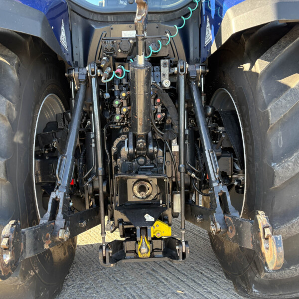 Close-up view of tractor rear hydraulics and three-point hitch with hoses and levers,