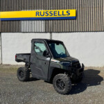Gray Polaris Ranger off-road utility vehicle in a gravel lot in front of a corrugated metal building with a Russell sign.