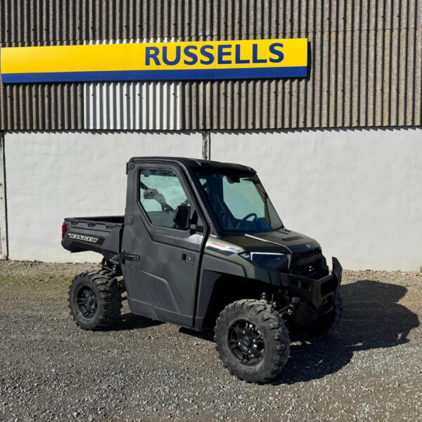 Gray Polaris Ranger off-road utility vehicle in a gravel lot in front of a corrugated metal building with a Russell sign.