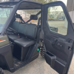 Open door of a black off-road vehicle, showing the front bench seat and safety belts inside the cabin.