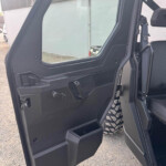 Open black off-road SUV door showing a rugged plastic interior panel, window frame, and visible seat belt near the doorway outside landscape.