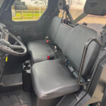 Interior of a utility vehicle with a two-seat bench, left-side steering wheel, and visible seat belts in use.