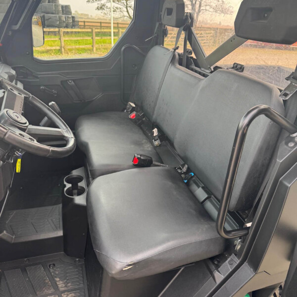 Interior of a utility vehicle with a two-seat bench, left-side steering wheel, and visible seat belts in use.