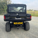 Rear view of a Polaris off-road pickup with a large open cargo bed, UK registration plate YX20 AYE, rugged tires, in a rural gravel lot.