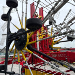 Close-up of a red multi-row farm implement with yellow supports, black wheels, and many metal tines outdoors