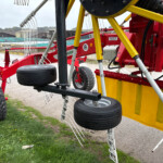 Close-up of a red and yellow farming sprayer with large black tires and metal framework outdoors.