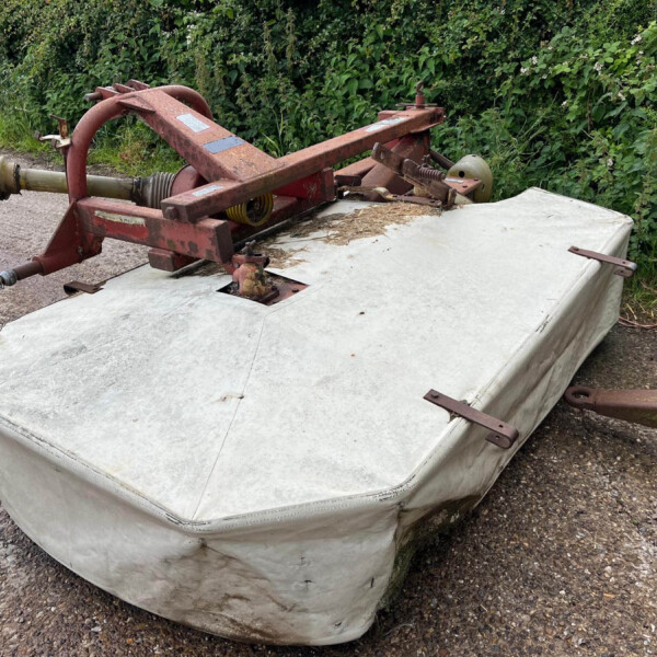 Old, rusted red farm implement resting on a white tarp-covered platform outdoors beside a gravel path and green shrubbery in the background if this image is about equipment in a yard.