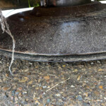 Close-up of a dusty black circular metal surface with a frayed rope hanging on the left, outdoors on a gravel ground.