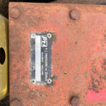 Close-up of a rusted red metal surface with four hex bolts and a small black-and-white label, yellow edge on the left, and a dark cavity in the background.