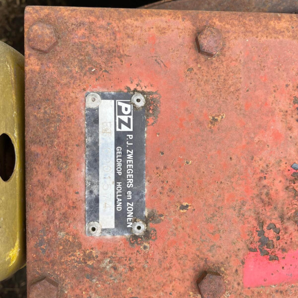 Close-up of a rusted red metal surface with four hex bolts and a small black-and-white label, yellow edge on the left, and a dark cavity in the background.