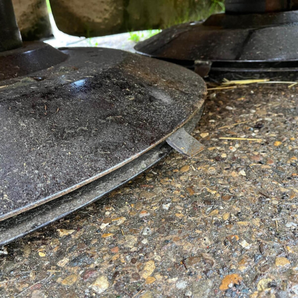 Close-up of dirty black metal wheels resting on a pebbled ground, with hints of green vegetation in the background.