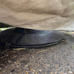 Underside of a light fabric cover draped over a round black platform outdoors, with dirt and small rocks visible nearby.