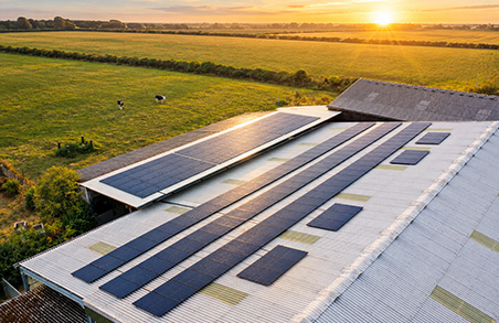 Solar panels installed on a sloped metal roof overlooking a rural field at sunset, forming a rooftop solar array in the warm light.