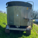 Large metal industrial tank on a trailer parked on grass beside a building, with a UK flag sticker and hazard signs visible.